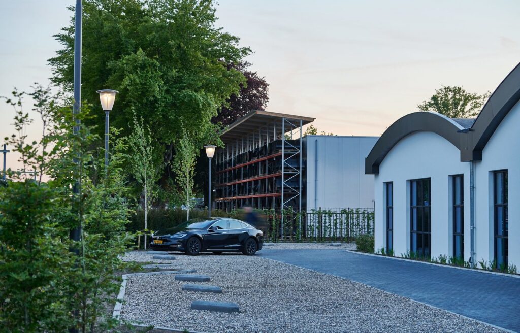 Kvällsbild med två moderna gatlampor som sprider ett varmt, jämnt sken över gång- och parkeringsytor, illustrerar PROLJUS AB:s energieffektiva och väderbeständiga armaturer för bostads- och företagsmiljöer, kontakta PROLJUS AB för offert