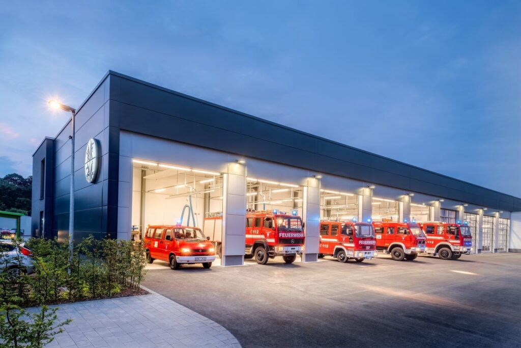 Brandstationsfasad i skymning där PROLJUS ABs slimmade takarmaturer ger jämnt och klart LED‑ljus över öppna portar och brandbilar, förbättrar säkerhet, driftsekonomi och professionell estetik för räddningstjänster PROLJUS AB