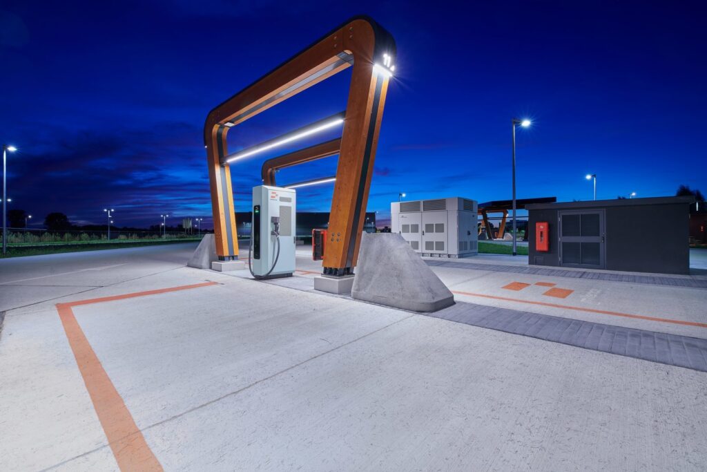 Moderna LED-armaturer integrerade i böjda träbågar belyser en elbilsladdningsstation i skymningen, ger jämnt, energieffektivt och attraktivt ljus som framhäver design och trygghet PROLJUS AB