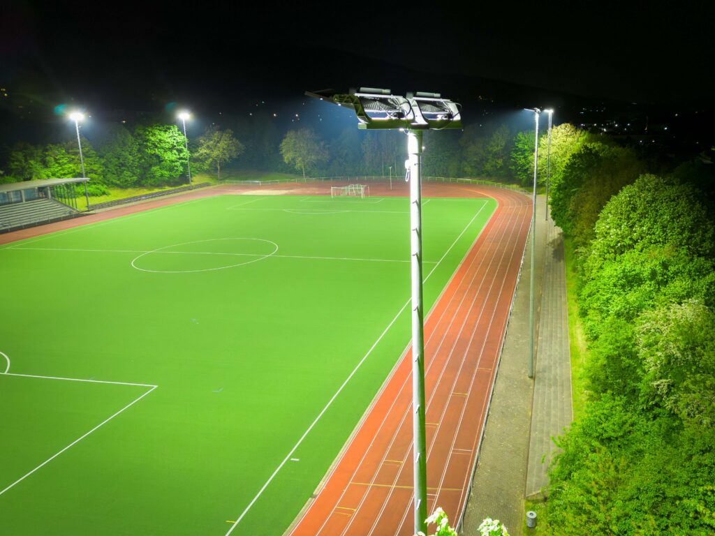 Nattbild av en sportsarena upplyst av högt monterade, energieffektiva PROLJUS AB:s LED-armaturer som ger stark, jämn och bländfri belysning över konstgräsplan och löparbana, robust utomhusdesign för professionell sportanläggning