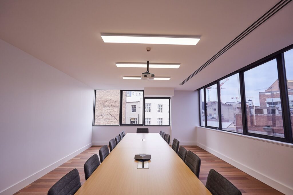 Konferensrum med långa rektangulära takarmaturer från PROLJUS AB som ger jämnt varmvitt och energieffektivt ljus över bordet, perfekt för moderna kontor och mötesrum