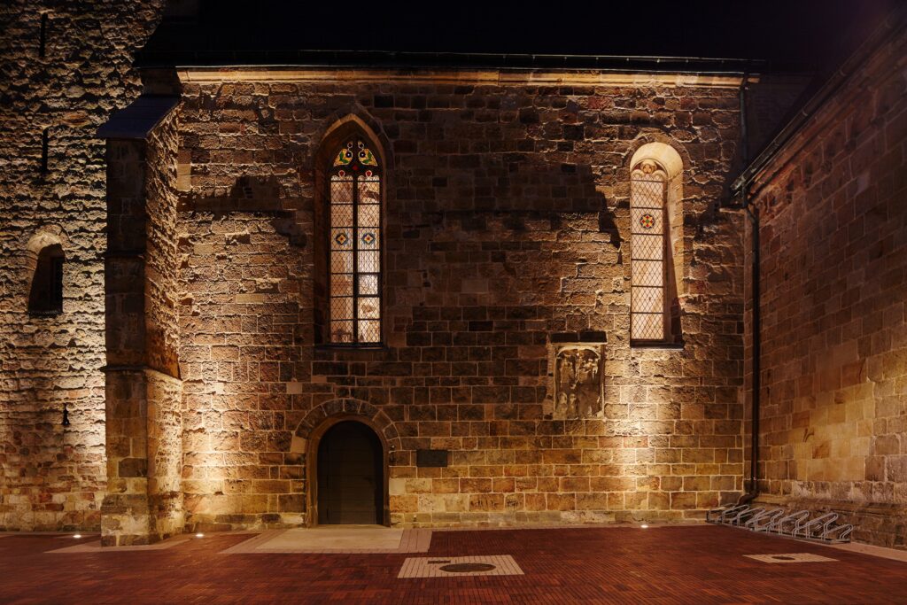 Nattbild av en stenfasad upplyst med armaturer från PROLJUS AB som varmvitt framhäver stenstruktur glasmålade fönster och entré och visar energieffektiv trygg arkitekturbelysning som stärker fastighetens visuella värde