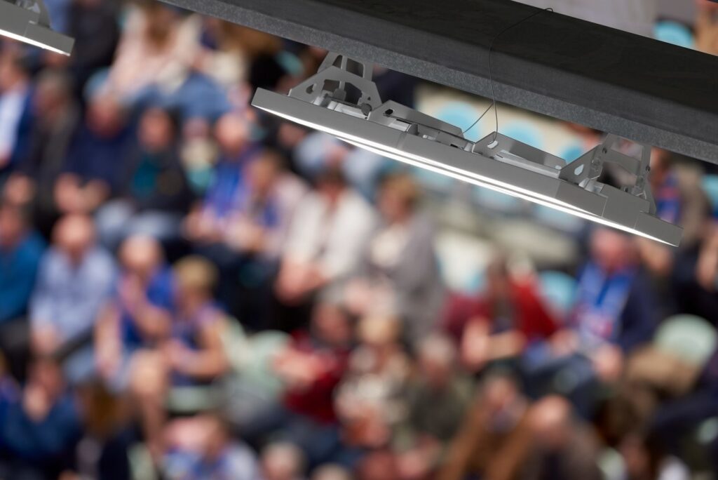 Närbild på modern takmonterad LED-armatur från PROLJUS AB som levererar kraftfullt energieffektivt ljus och robust design över en suddig arenapublik perfekt för sportarenor och evenemang