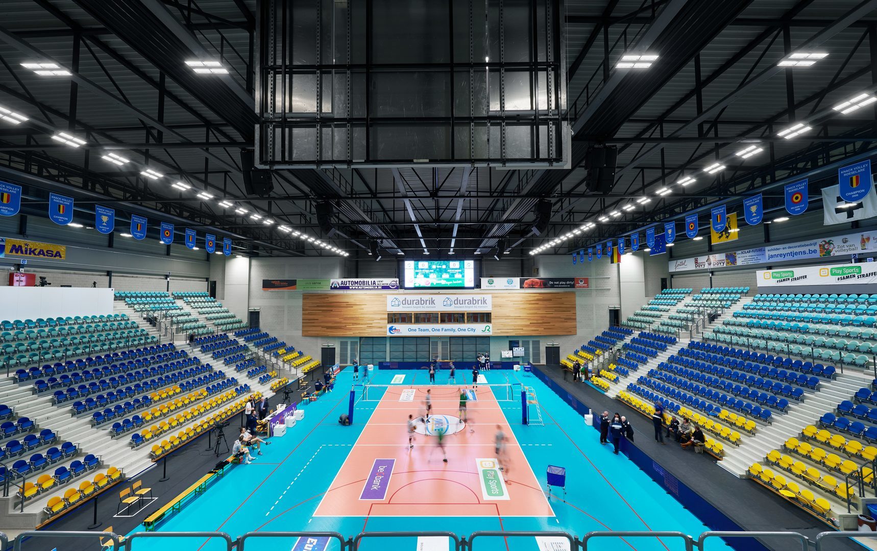 Takupphängda linjära LED-armaturer i rader över en modern inomhusarena som ger stark, jämn och bländfri belysning över spelplan och läktare — perfekt exempel på PROLJUS ABs energieffektiva och högpresterande belysningslösningar