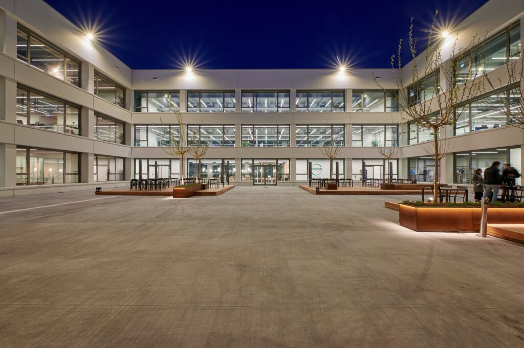 Nattbild av en modern kontorsinnergård där PROLJUS ABs armaturer syns tydligt med stjärnformade fasadbelysningar och slanka LED-lyslister i fönstren som levererar jämn, energieffektiv och arkitekturframhävande belysning perfekt för kommersiella miljöer