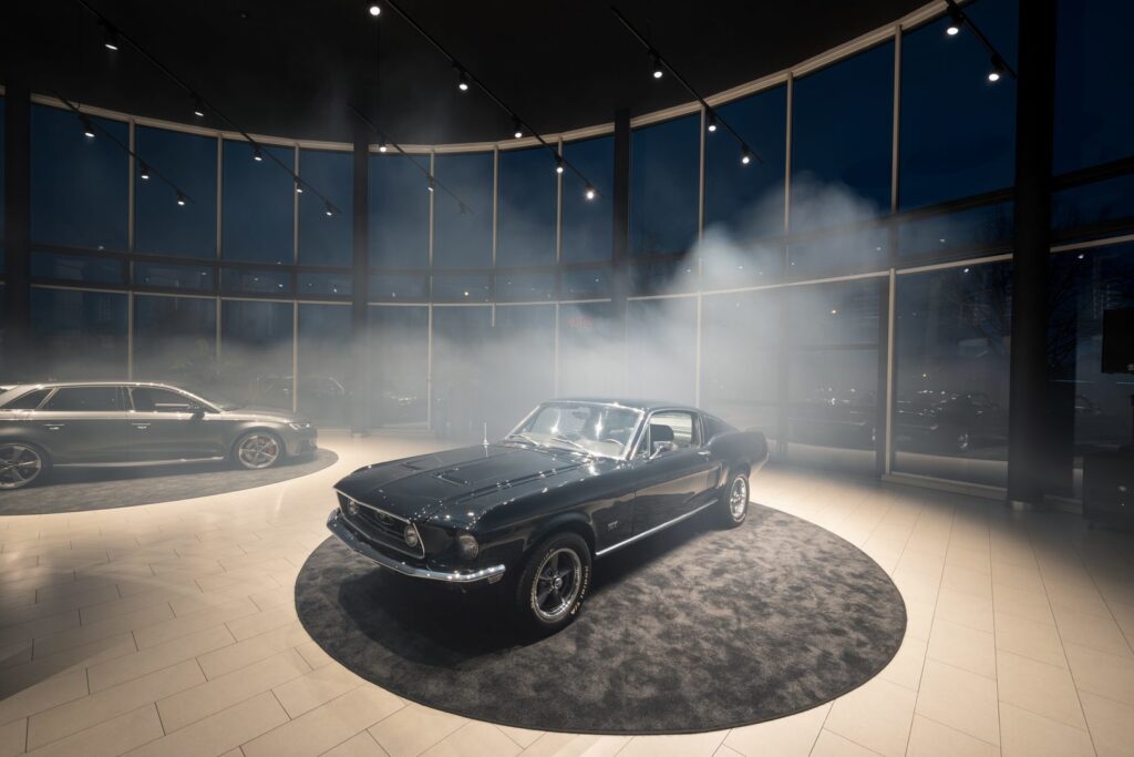 Showroom med klassisk Mustang upplyst av spårmonterade spotlights och riktade takarmaturer från PROLJUS AB som levererar kontrollerat ljus, jämn färgåtergivning och skarpa kontraster i en rökig atmosfär, kontakta PROLJUS AB för skräddarsydd showroombelysning