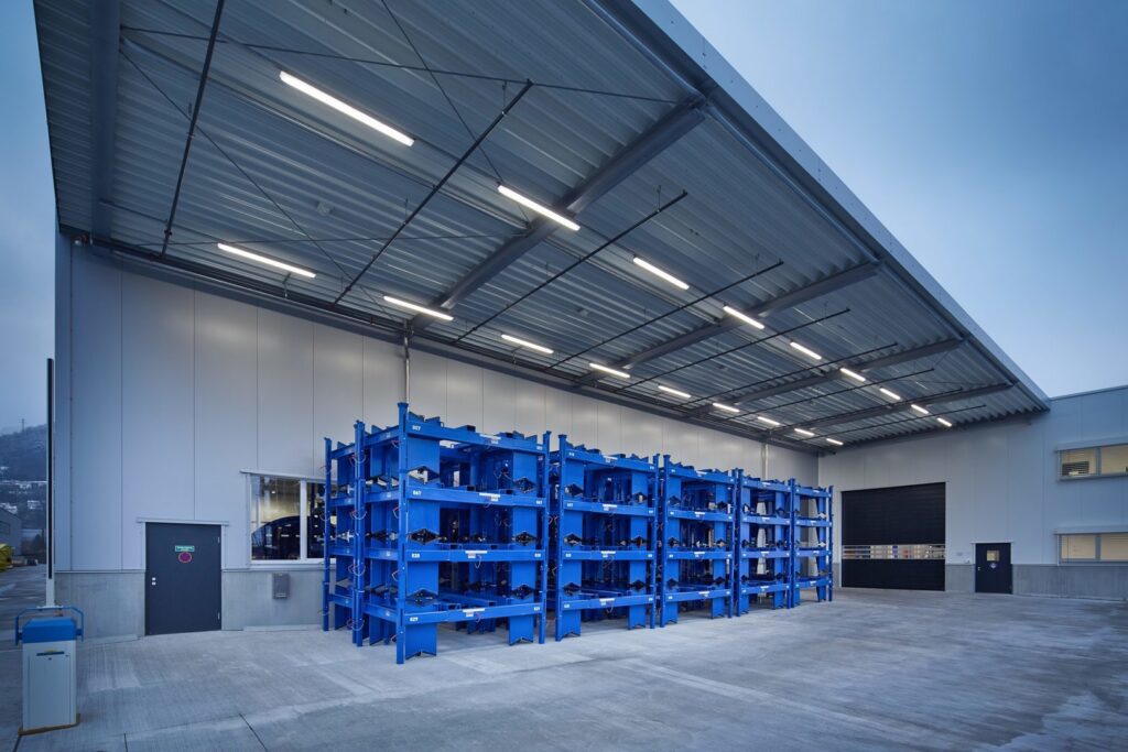 Modern industrimotiv med PROLJUS AB:s långa LED-armaturer monterade i taket över ett upplyst lastkajsområde, jämn och kraftfull belysning som framhäver ytor och skapar en trygg arbetsmiljö, energieffektiva och robusta armaturer idealiska för lager och produktion