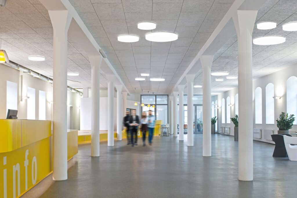Runda ytmontade takarmaturer i varierande storlekar dominerar taket och sprider klart, jämnt och energieffektivt dagsljusliknande ljus i en öppen receptions- och kontorshall, en stilren modern design med hög ljusspridning från PROLJUS AB