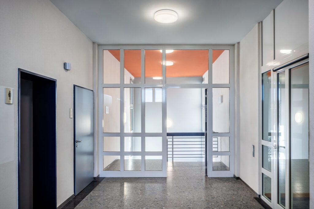 Entréhall belyst av PROLJUS ABs runda takarmaturer och vägglampor som sprider mjukt, jämnt och bländfritt ljus, en stilren och energieffektiv belysningslösning för trapphus och offentliga utrymmen