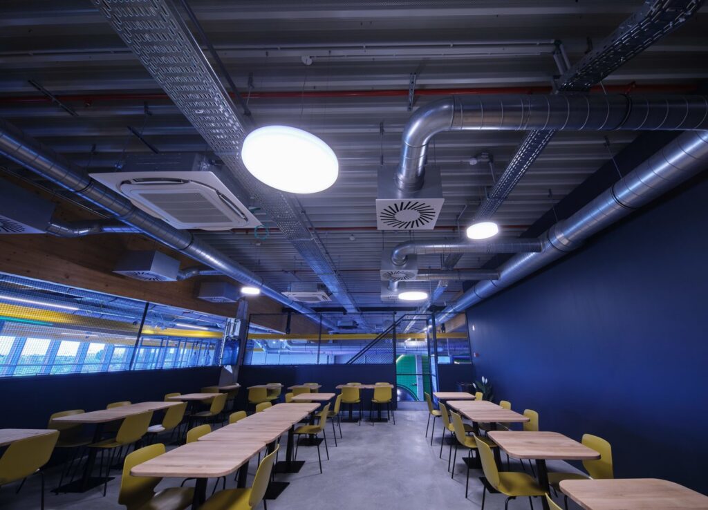 Takmonterade runda LED-armaturer och inbyggda ventilationsdon i en modern industrimatsal, jämnt kallvitt ljus och energieffektiv design som visar kvaliteten i PROLJUS ABs belysningslösningar