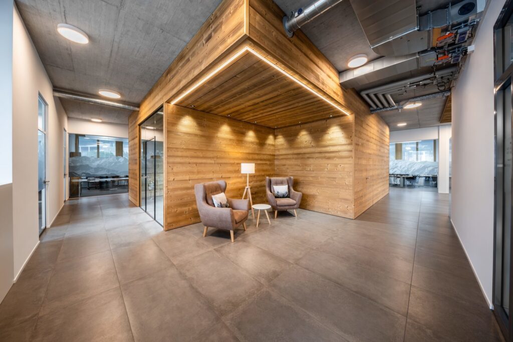 Kontorsentré med träklädd samtalsnisch upplyst av PROLJUS ABs LED-lösningar: infällda spotlights i taket, linjär LED-stripe som ramar in nischen och cirkulära takarmaturer som skapar varm, energieffektiv och installationsvänlig belysning perfekt för moderna arbetsmiljöer