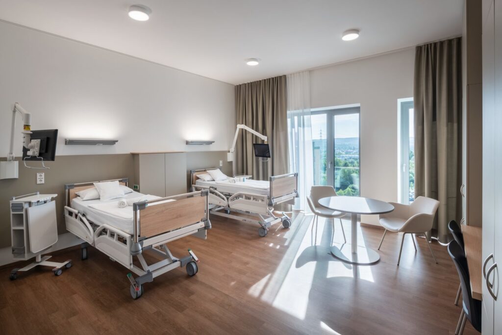 Modern sjukhussal upplyst av tre infällda takarmaturer och två väggarmaturer som ger mjukt, jämnt LED-ljus och skapar en lugn, hygienisk vårdmiljö med energieffektiva, lättstädade armaturer från PROLJUS AB