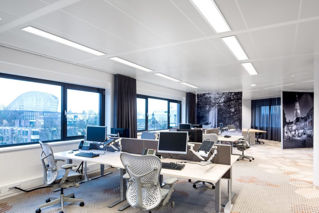 Öppet modernt kontorslandskap upplyst av långa, infällda och energieffektiva LED‑armaturer i taket som ger jämnt, bländfritt arbetsljus och förbättrad ergonomi, en idealisk belysningslösning från PROLJUS AB