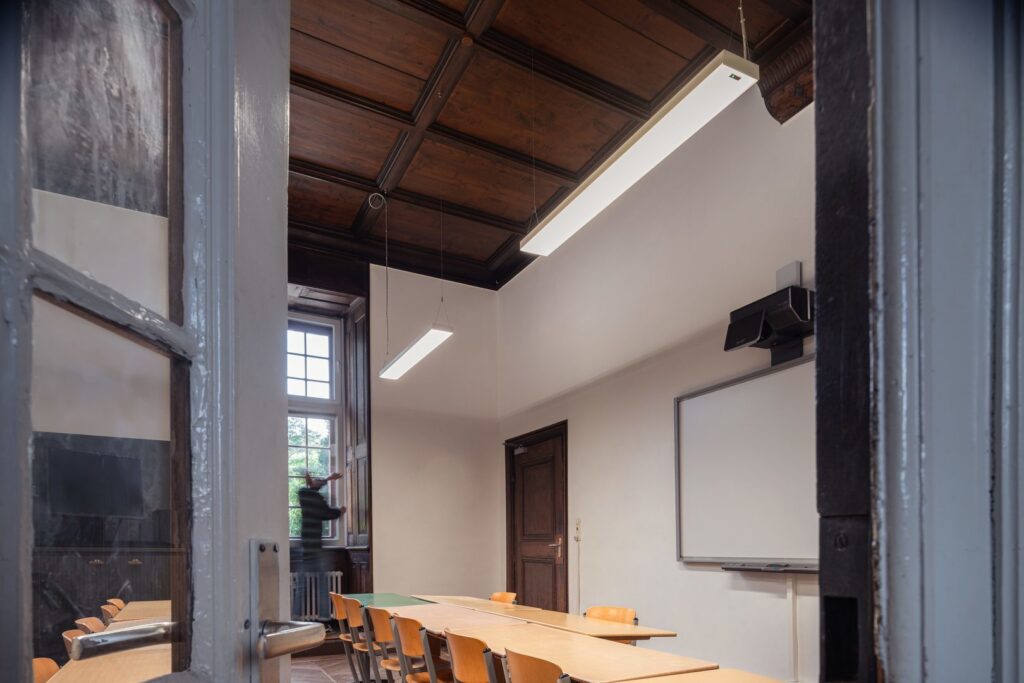 Två upphängda linjära LED-armaturer från PROLJUS AB i ett klassrum med träpanelstak, elegant och energieffektiv belysning som ger jämnt ljus, enkel installation och perfekt för skolor och kontor