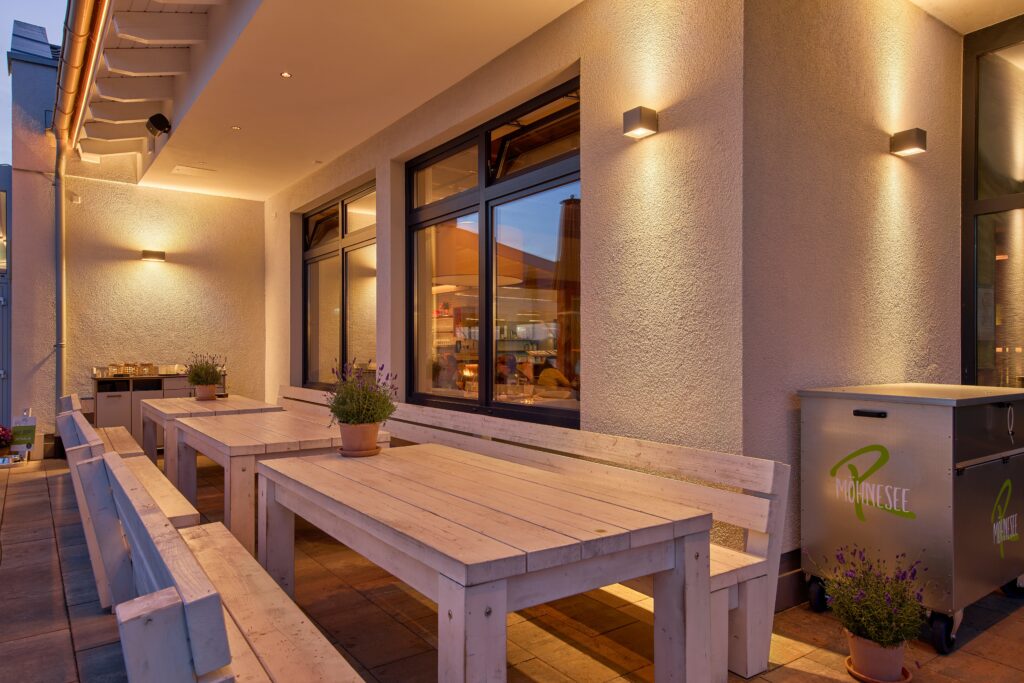 Mysig uteservering på restaurang med träbord, lavendelkrukor och varm fasadbelysning i skymningen.