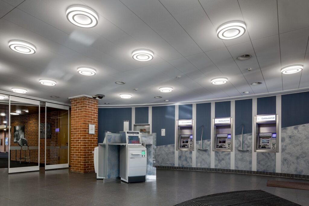 Centralt fokus på flera cirkulära ringformade LED-takarmaturer från PROLJUS AB som sprider mjukt, bländfritt och energieffektivt ljus i en modern bankentré, elegant design som lyfter kommersiella miljöer och inspirerar köp