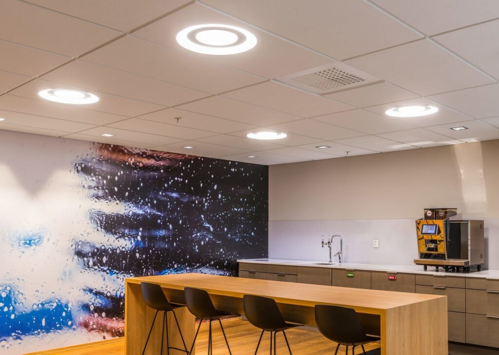 Infällda runda LED-armaturer från PROLJUS AB i ett modernt företagskök som sprider mjukt, jämnt och bländfritt arbetsljus över träbord och sittplatser, energieffektiva och stilrena belysningslösningar för kontor och pausutrymmen — välj PROLJUS AB för kvalitet och design