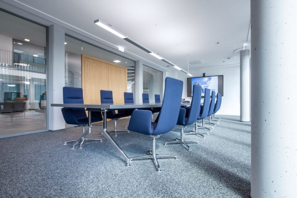 Slanka linjära LED-pendelarmaturer från PROLJUS AB lyser jämnt och bländfritt över ett modernt konferensbord, optimal lösning för professionella kontorsmiljöer