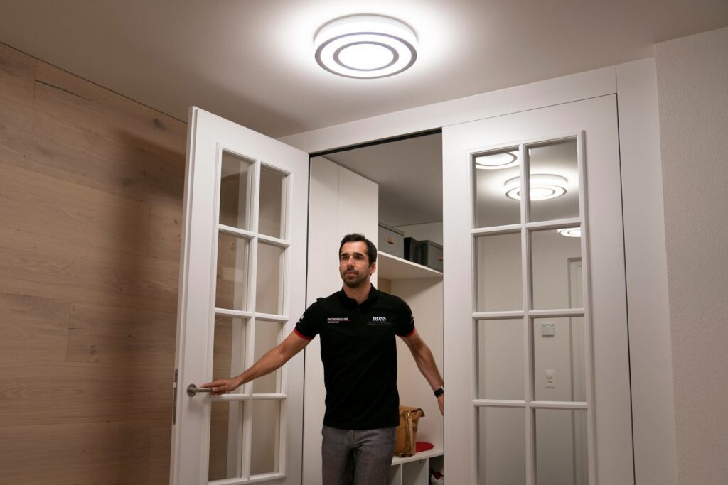 Modern cirkulär LED-takarmatur från PROLJUS AB som sprider mjukt, jämnt och energieffektivt ljus i en entré, reflekteras i glasdörrar och framhäver trä- och vita ytor, idealisk för hem och kontor