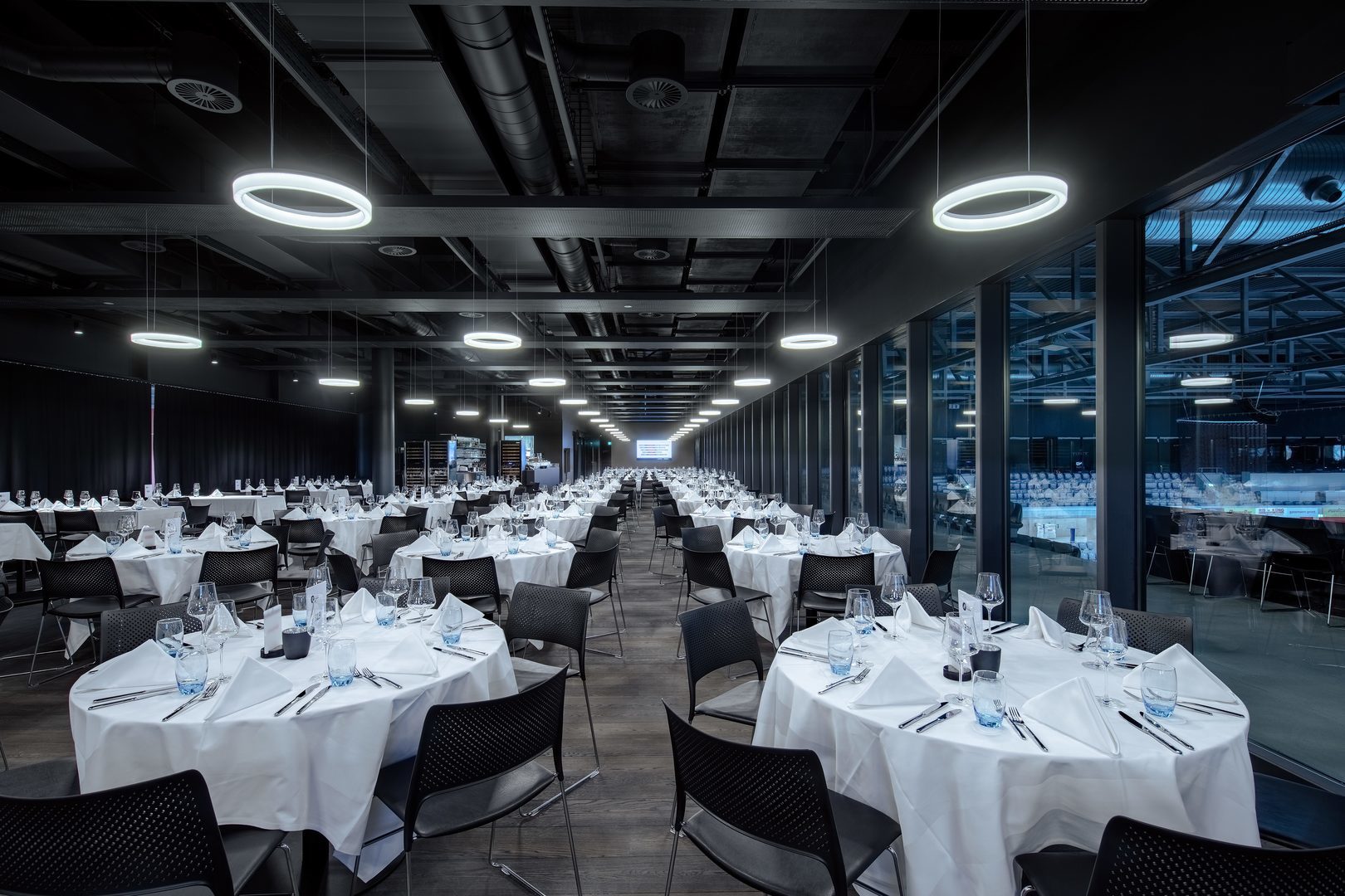 Större bankettlokal belyst av eleganta cirkulära hängande LED armaturer från PROLJUS AB som ger jämnt energieffektivt kallvitt ljus över dukade bord och skapar en modern inbjudande atmosfär perfekt för evenemang