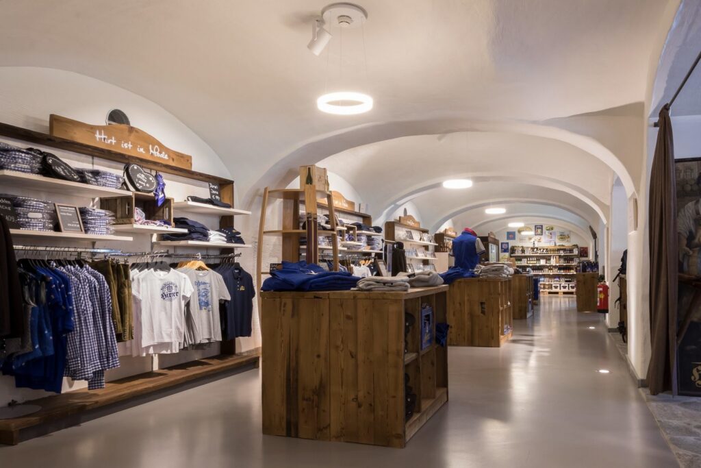 Ringformade pendellampor och infällda spotlights i ett valvformat butikstak som ger jämnt, varmt ljus över varor och trädisplayer, belysning från PROLJUS AB som framhäver produkter och erbjuder energieffektiva lösningar