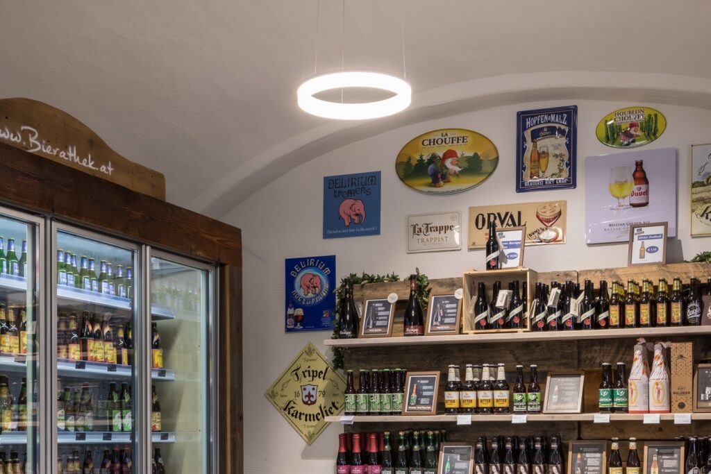 Ringformad hängande LED-armatur från PROLJUS AB lyser mjukt och jämnt över hyllor med hantverksöl och skyltar i en butik och framhäver produkter samtidigt som den skapar en inbjudande atmosfär som ökar försäljningen