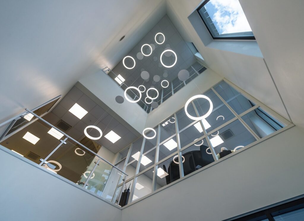 Hängande cirkulära LED-armaturer i varierande storlekar som sprider mjukt energieffektivt ljus i ett modernt atrium med glasade kontorsytor, elegant belysningslösning från PROLJUS AB