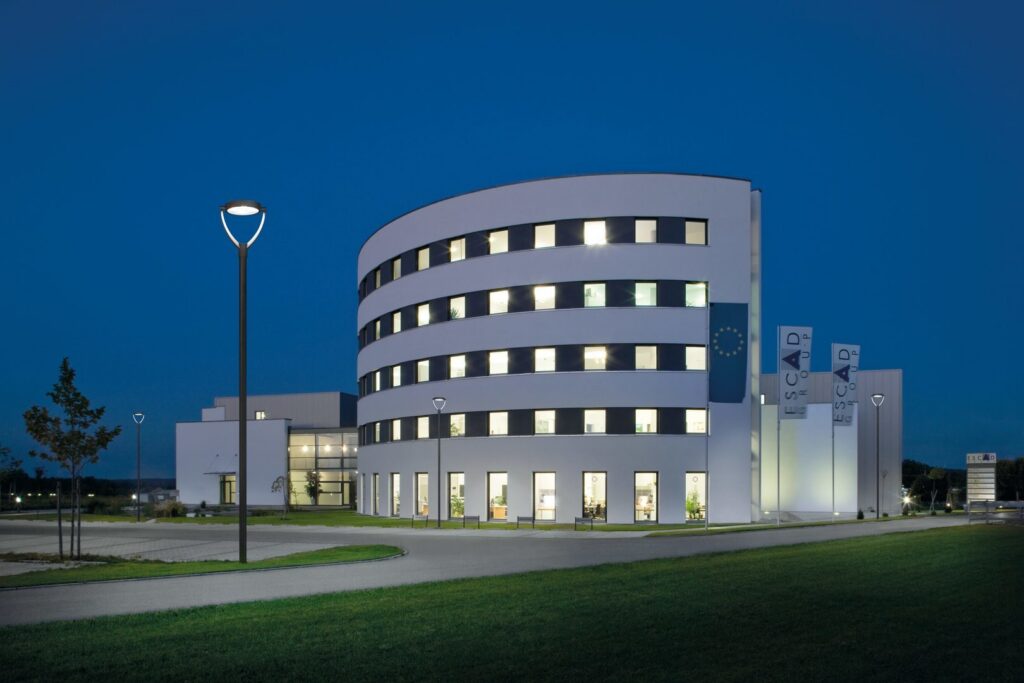 Snygga energieffektiva armaturer från PROLJUS AB i förgrunden som med jämnt vitt LED-ljus belyser en rund kontorsbyggnad i skymningen och skapar en säker och inbjudande atmosfär idealisk för företagsinstallationer