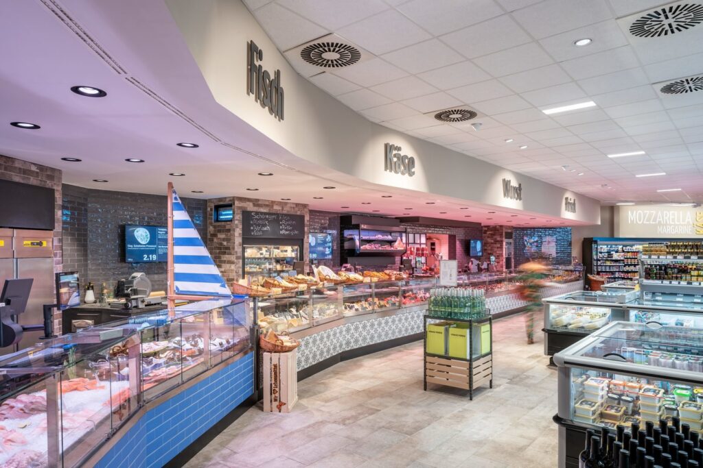 Interiör i livsmedelsbutik med moderna infällda downlights och LED-paneler från PROLJUS AB som ger jämn energieffektiv belysning och accentuerar diskar och varor för en inbjudande atmosfär som höjer försäljningen