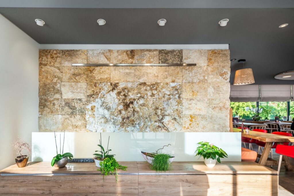 Interiör med flera infällda spotlights i taket, en slank linjär väggarmatur som framhäver naturstensväggen och en dekorativ pendellampa över matplatsen, högkvalitativa och energieffektiva ljuslösningar från PROLJUS AB som skapar atmosfär och modern design