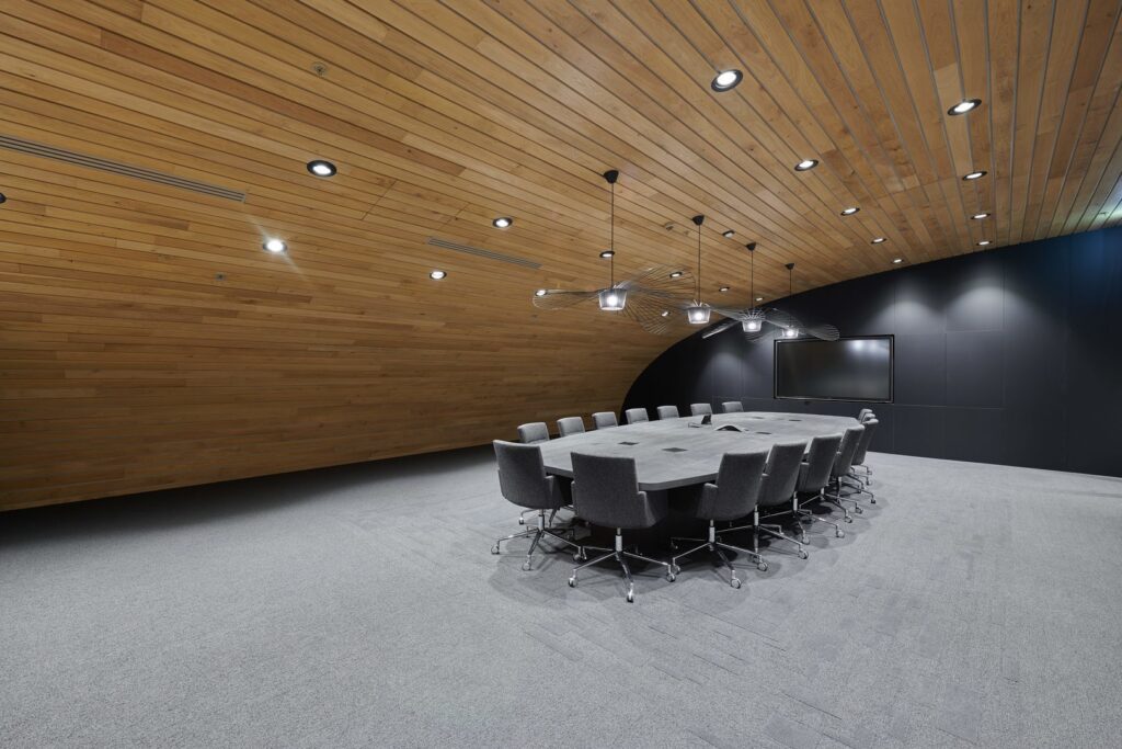 Konferensrum belyst av PROLJUS ABs skulpturala pendlar i trådram över bordet och infällda LED‑spotlights i träpaneltaket som ger jämnt, energieffektivt ljus och en modern, säljande atmosfär för företag