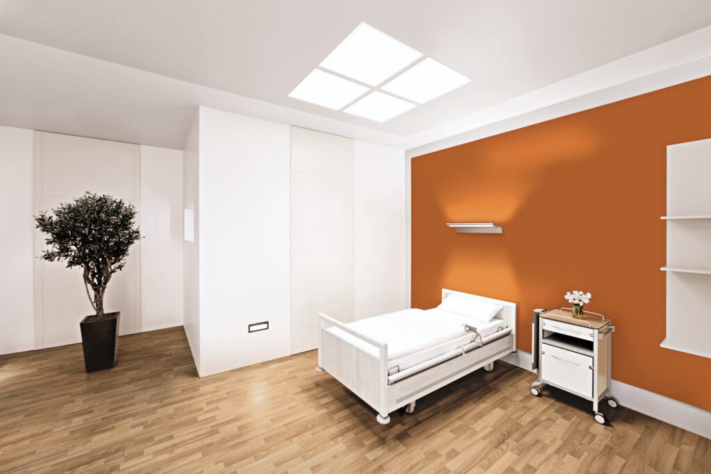 Vitt modernt patientrum med kvadratisk infälld LED-takbelysning och väggmonterad lampa över sängen som ger jämnt varmt ljus, förbättrar orientering och trivsel och visar PROLJUS ABs energieffektiva belysningslösningar
