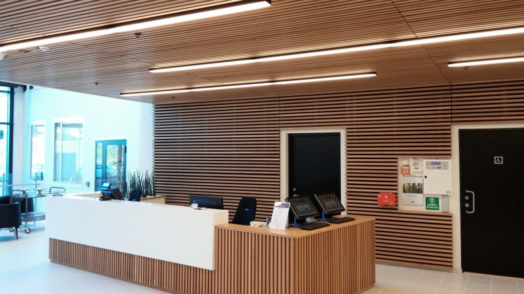 Reception med lamelltak i trä och långa linjära LED-armaturer som ger jämnt, varmt ljus och visar PROLJUS ABs energieffektiva belysningslösningar för kontor och entréer