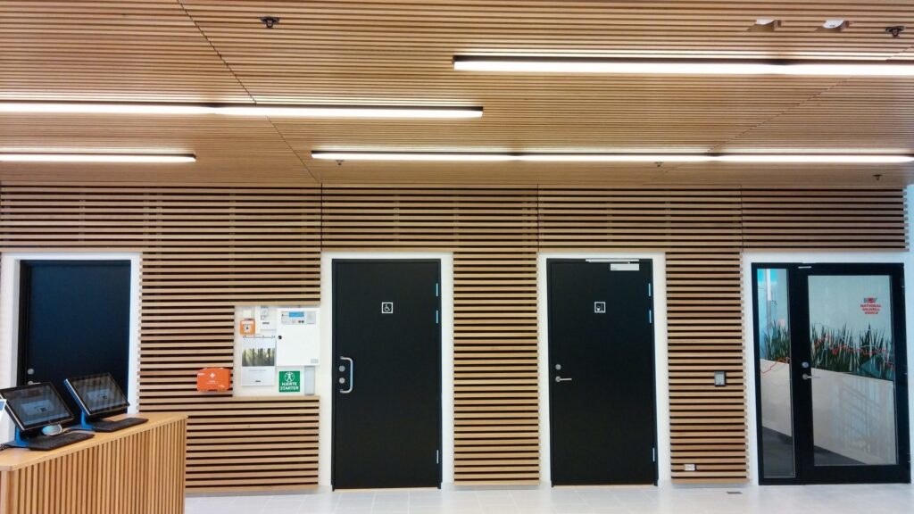 Linjära LED-armaturer från PROLJUS AB integrerade i träpaneltaket som skapar varmt, jämnt och energieffektivt allmänljus i en modern entré, idealiska för kontor och offentliga ytor — kontakta PROLJUS AB