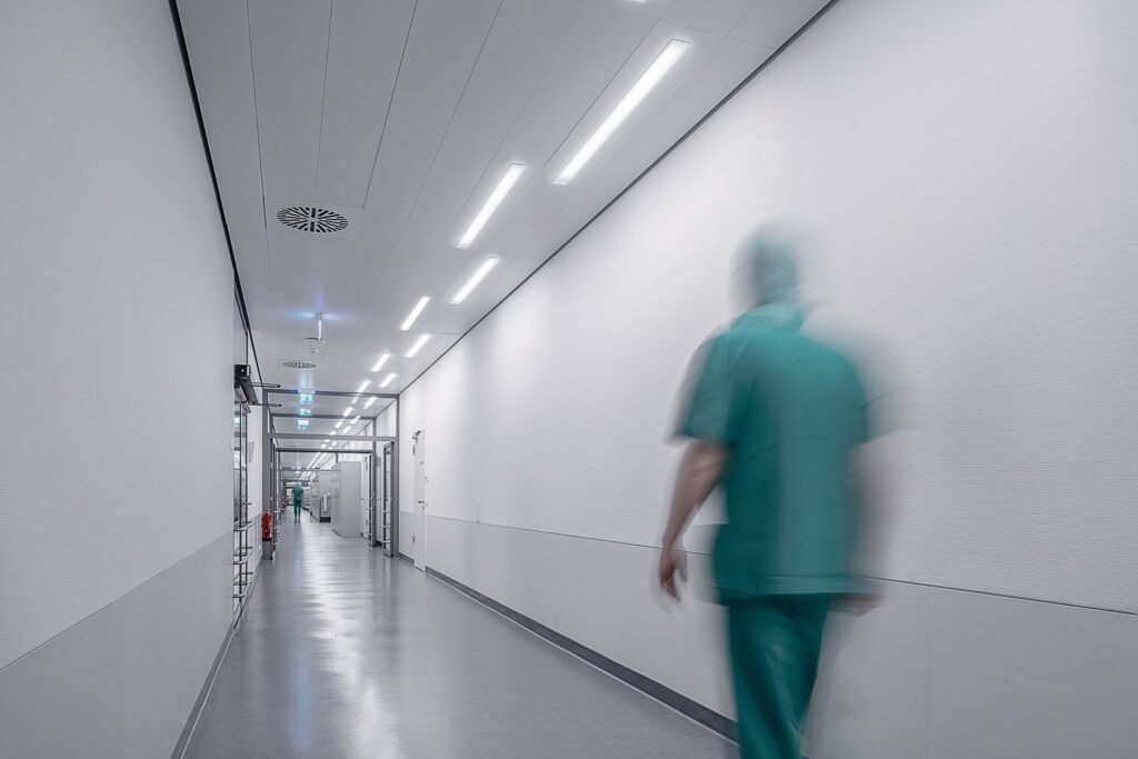 Lång vit sjukhuskorridor med rad av moderna infällda LED‑armaturer i taket som ger jämnt bländfritt och energieffektivt ljus, förstärker säkerhet och arbetskomfort i vårdmiljöer och erbjuds av PROLJUS AB
