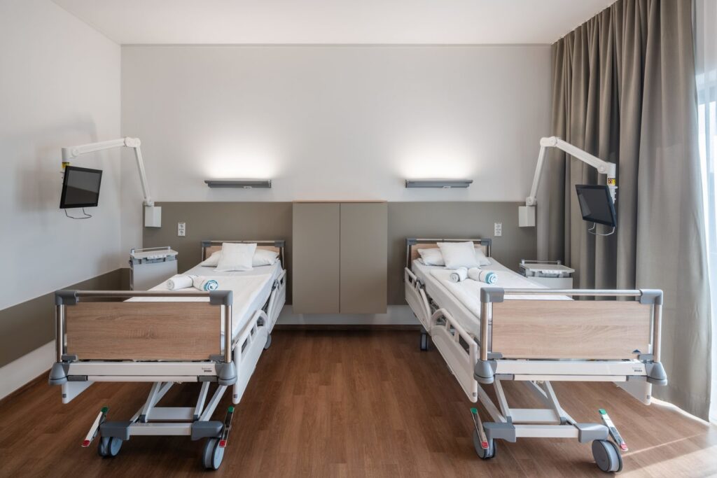 Två väggmonterade armaturer från PROLJUS AB ovanför varsin sjukhussäng som ger mjuk, bländfri upp- och nedåtriktad LED-belysning i varm ton, modern skandinavisk design som ökar trivsel och energieffektivitet