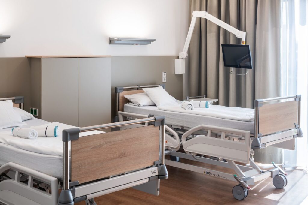 Sjukhussal med PROLJUS ABs moderna väggmonterade LED-armaturer ovanför sängarna som ger jämnt, bländfritt varmvitt ljus, energieffektiva och dimbara med lättstädade hygieniska ytor, stilren design som förbättrar patientsäkerhet och arbetsmiljö