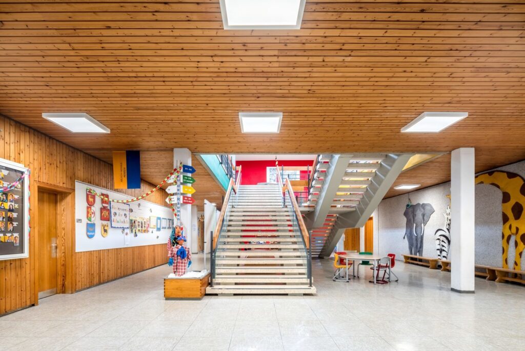 Skolentré med träpaneltak och flera kvadratiska infällda LED-armaturer som ger jämn, bländfri och energieffektiv allmänbelysning, en modern och diskret belysningslösning från PROLJUS AB