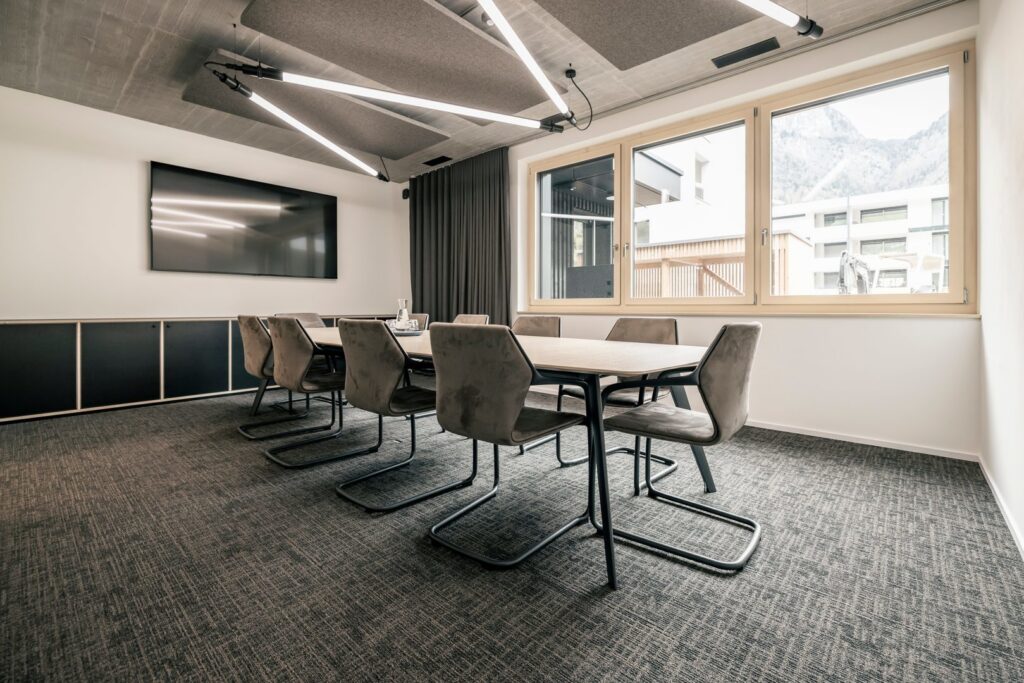 Modernt konferensrum med geometriska korsande linjära LED-armaturer i taket som ger jämnt, energisnålt ljus och förhöjer arbetsmiljön, högkvalitativ kontorsbelysning från PROLJUS AB