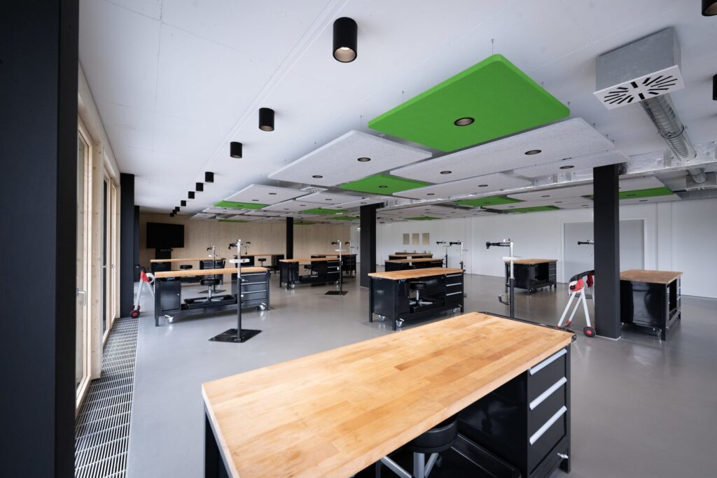 Modern verkstad med svarta cylinderformade takarmaturer och gröna och grå akustikpaneler med infällda LED-spotlights, energieffektiv, jämn och skuggfri arbetsbelysning signerad PROLJUS AB som förhöjer produktivitet och arbetsmiljö