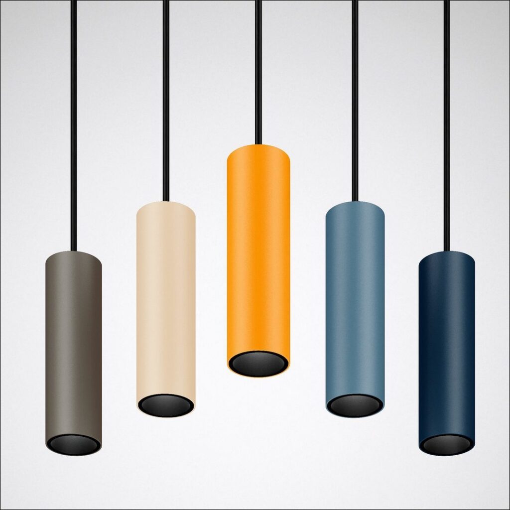 Fem cylindriska pendellampor i matt pulverlack i antracit, beige, orange, ljusblå och mörkblå hängande i svarta kablar mot ljus bakgrund, stilren modern design för restaurang, kontor eller kök från PROLJUS AB