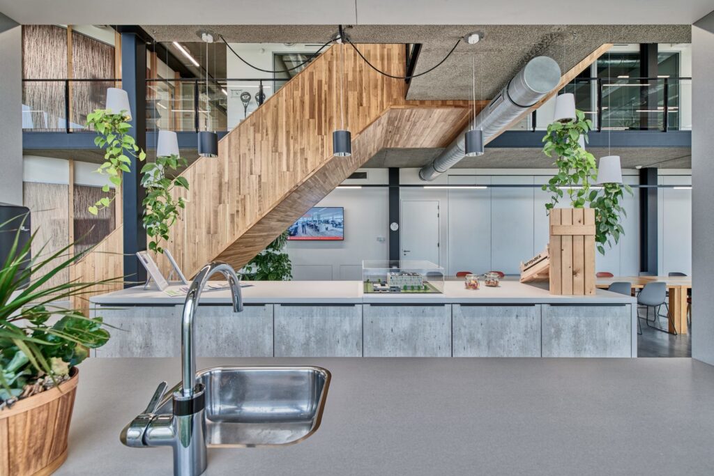 Modernt kontorslandskap upplyst av eleganta hängande armaturer — svarta cylindriska pendlar som ger riktat arbetsljus och vita skärmar omgivna av hängande växter för extra atmosfär, perfekt för kontor och showrooms, kontakta PROLJUS AB