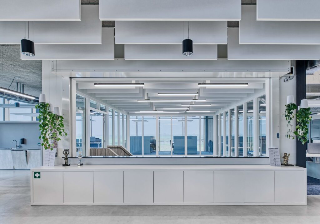 Modernt kontorslandskap belyst av PROLJUS AB:s högkvalitativa takarmaturer med svarta cylinderpendlar och integrerade linjära LED-armaturer i vita akustikbafflar som ger jämnt, energieffektivt arbetsljus och en stilren estetik