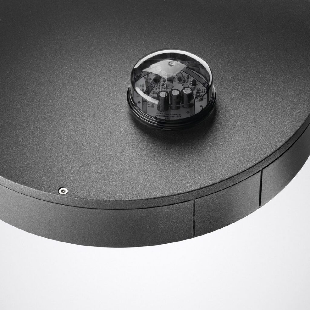 Närbild på en rund svart metallarmatur med strukturerad yta och en integrerad sensor/drivermodul under en klar kupa, modern och robust design från PROLJUS AB för energieffektiv kommersiell belysning